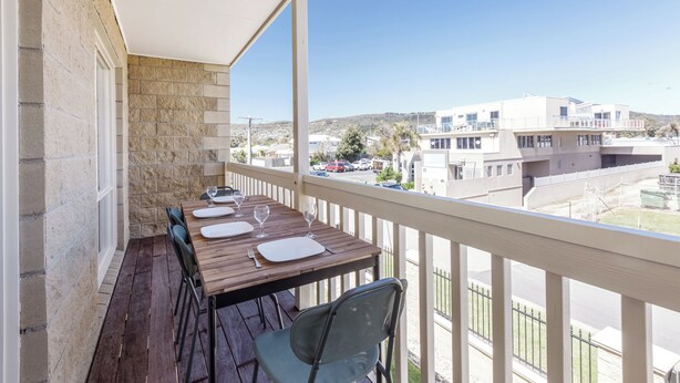 Un balcón con una mesa de madera dispuesta para comer, un muro de piedra y vistas a edificios y una calle.