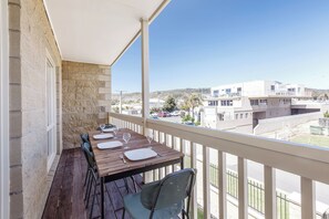 A balcony with a wooden table set for dining, a stone wall, and a view of buildings and a street. - Sea Quinn Escape Steps to Dromana Beach and Dining (Dromana)