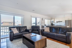 A modern living room with two leather sofas, a coffee table, and large windows offering a view of the city. - Sea Quinn Escape Steps to Dromana Beach and Dining (Dromana)