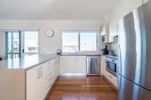 A modern kitchen with a stainless steel refrigerator, a dishwasher, and a large window providing natural light. - Sea Quinn Escape Steps to Dromana Beach and Dining (Dromana)