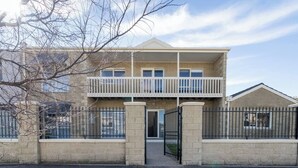 Un edificio residencial de dos pisos con un balcón en el nivel superior, entrada protegida por una reja y fachada de ladrillo.