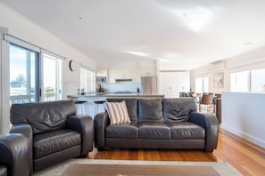 Ein modernes Wohnzimmer mit Ledersofa, Essbereich und einer Küche im Hintergrund.