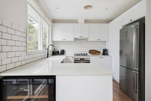 Eine moderne Küche mit weißen Schränken, einem Edelstahlkühlschrank, einem eingebauten Backofen und einem Fenster, das für natürliches Licht sorgt.