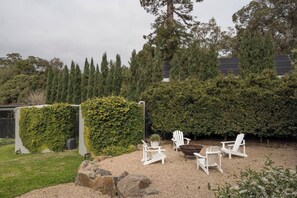 Un jardin agrémenté d’un espace détente, comprenant des chaises blanches et une table, le tout entouré d’une haie et d’arbres.