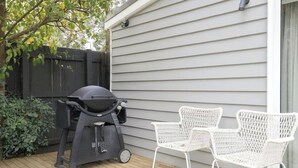 Eine Terrasse mit Grill und weißen Korbstühlen.