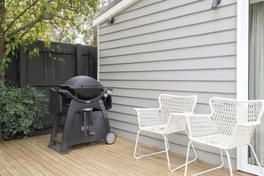 Eine Terrasse mit Grill und weißen Korbstühlen.