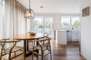 Ein Essbereich mit einem runden Holztisch, vier Stühlen, einer Pendelleuchte und Blick auf einen Balkon mit weißem Geländer.