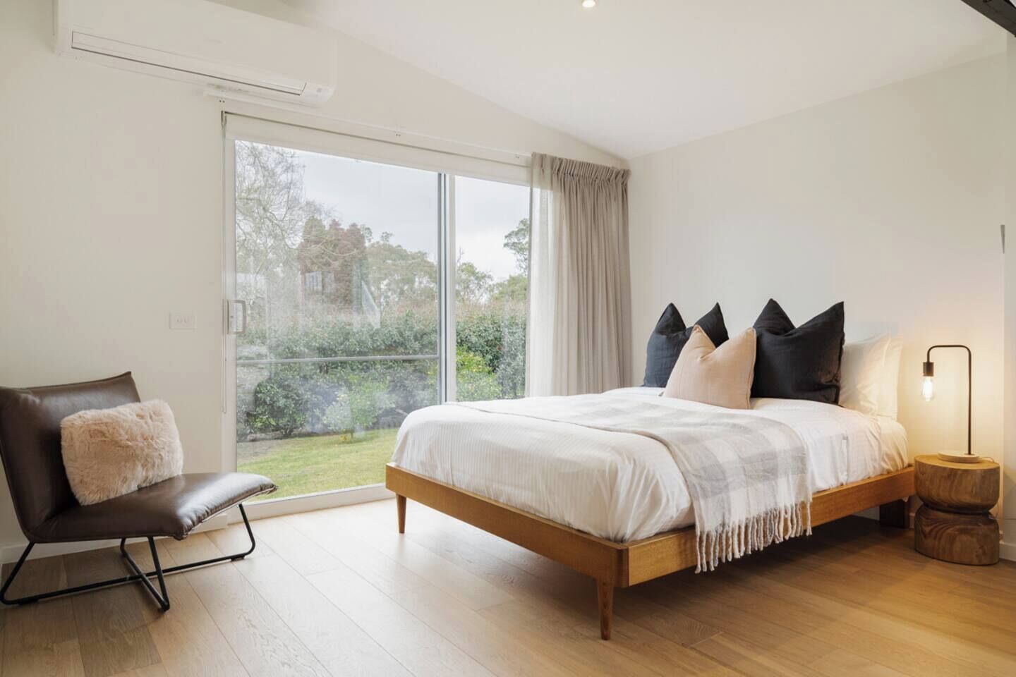 A bedroom with a large bed, a chair, a bedside table, and a view of the outdoors.