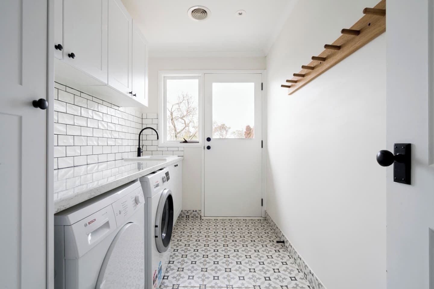 A laundry room with a washing machine, a drying rack, and patterned floor tiles.