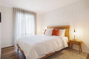 Une chambre d’hôtel avec un grand lit, une tête de lit en bois, une table de chevet avec une lampe et une fenêtre avec des rideaux.