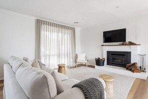Un salon moderne avec un canapé, une cheminée, un téléviseur et une grande fenêtre agrémentée de rideaux.