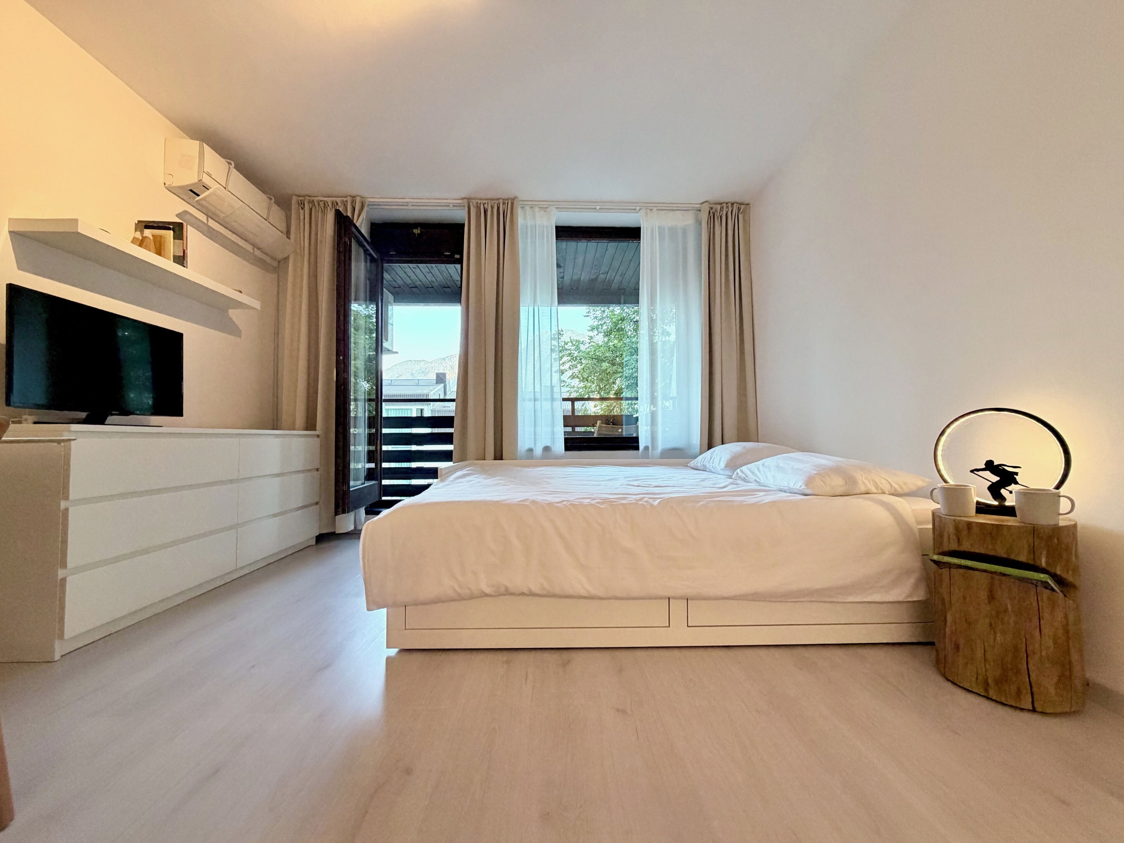 A modern bedroom with a bed, a TV, and a balcony with curtains.
