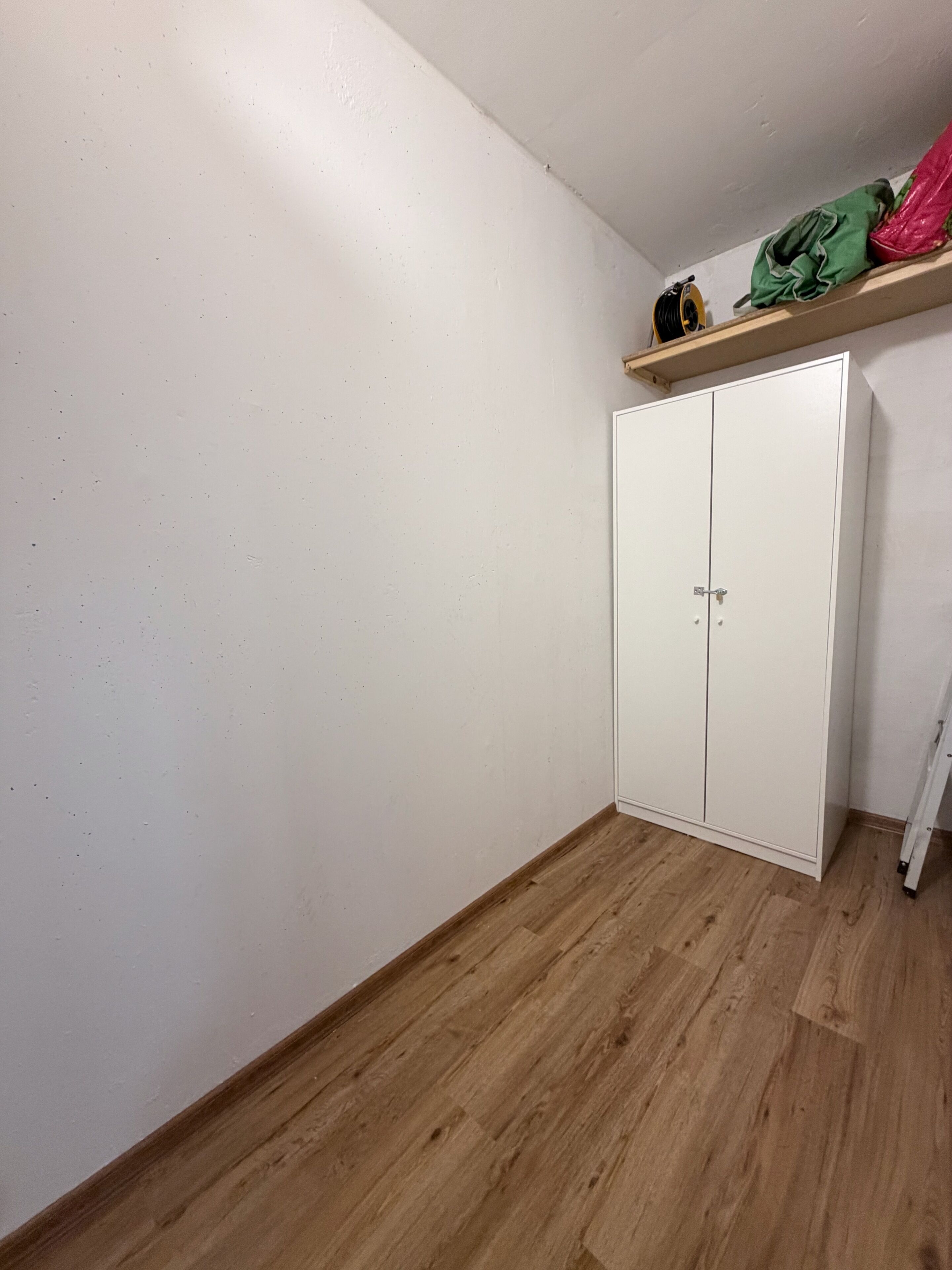 Une pièce avec un plancher en bois, des murs blancs et une armoire blanche à deux portes.
