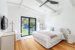A bedroom with a bed, bedside tables, a desk, a chair, a TV, and a sliding glass door to a backyard with a slide. - Pavilion Verde Designer Retreat near Rosebud Beach (Rosebud)