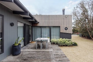 Ein modernes Haus mit Terrasse, Tisch und einer Topfpflanze.