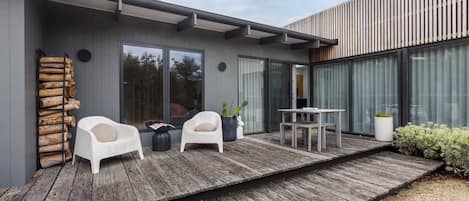 A modern outdoor deck with two white chairs, a small table, and a log display.