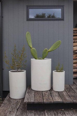 Three white planters with different plants on a wooden deck against a grey wall with a window. - Pavilion Verde Designer Retreat near Rosebud Beach (Rosebud)