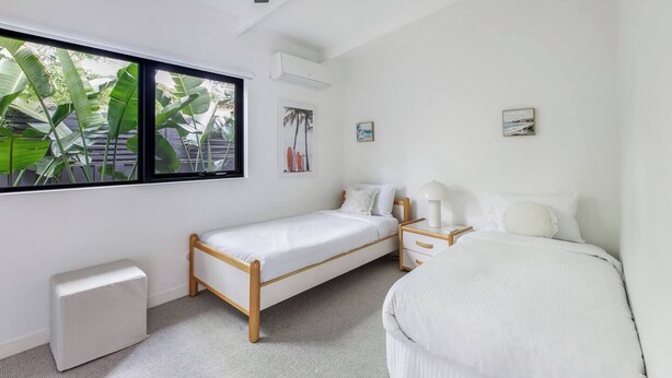 Un dormitorio con una cama individual, una mesita de noche, una ventana que ofrece vistas a zonas verdes y un ventilador de techo.