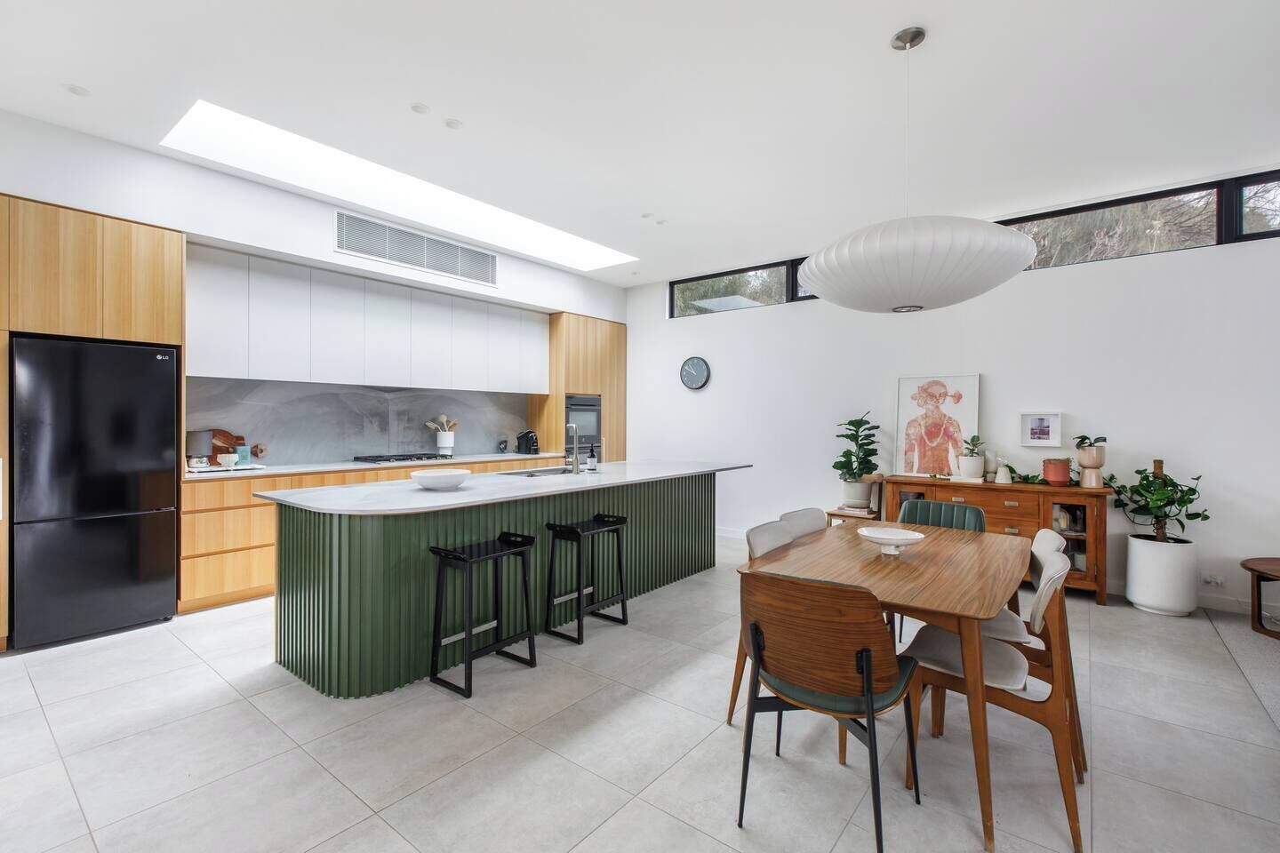 A modern kitchen with a central island, bar stools, and a dining area with a wooden table and chairs.