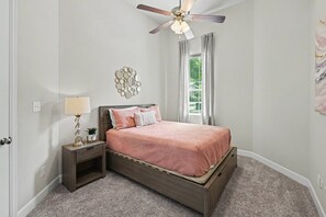A bedroom with a bed, nightstand, lamp, ceiling fan, and a decorative wall piece. - 5BR Lakefront Retreat | Pool + Hot Tub | Private Dock | Pet Friendly | Swim, Fish & Boat (Montgomery)