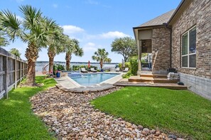 Un jardin avec une piscine, une terrasse en bois et une maison en briques.