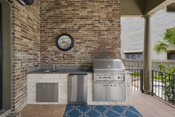 A compact outdoor kitchen with a built-in sink, a stainless steel grill, and a decorative clock on the wall. - 5BR Lakefront Retreat | Pool + Hot Tub | Private Dock | Pet Friendly | Swim, Fish & Boat (Montgomery)