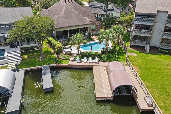 Un quartier résidentiel doté d’une piscine entourée de verdure, d’un quai et d’un bateau.