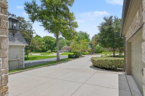 A residential driveway with a stone wall on the left, a garage on the right, and a well-maintained lawn with trees. - 5BR Lakefront Retreat | Pool + Hot Tub | Private Dock | Pet Friendly | Swim, Fish & Boat (Montgomery)
