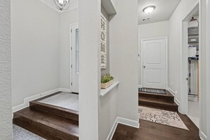 A clean, well-lit hallway with wooden steps, a white door, and a small plant on a shelf. - 5BR Lakefront Retreat | Pool + Hot Tub | Private Dock | Pet Friendly | Swim, Fish & Boat (Montgomery)