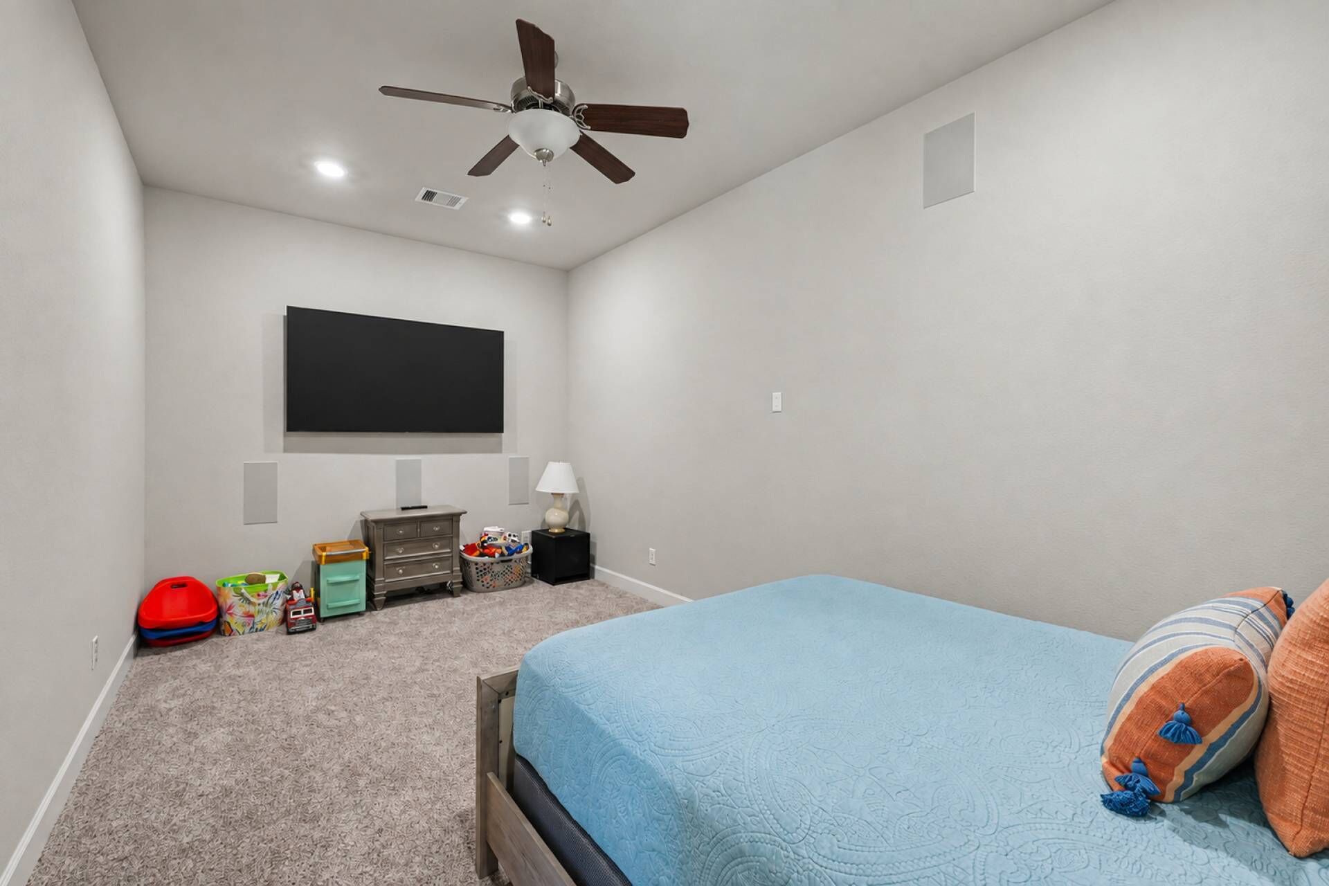 A bedroom with a bed, a ceiling fan, a TV mounted on the wall, and a small dresser.