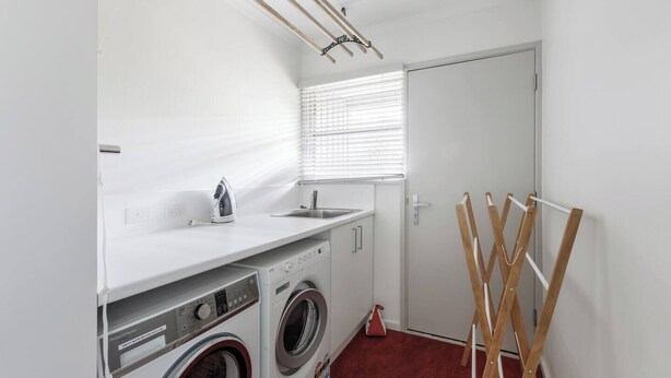 Een wasserette met een wasmachine, droger, strijkplank en een droogrek.