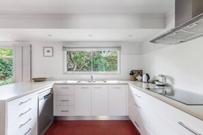 Eine moderne Küche mit weißen Schränken, einer doppelten Spüle und einem Fenster mit Blick auf Grünflächen.