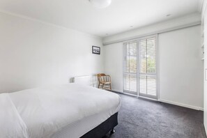 Ein Schlafzimmer mit Bett, Sessel, Heizkörper und einem Fenster mit Jalousien.