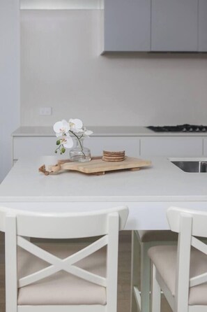 A modern kitchen with a white countertop, a vase with white flowers, and a wooden cutting board. - Bayside Calm Walk to Mornington Foreshore and Dining (Mornington)