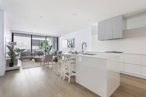 A modern kitchen with a central island, white cabinetry, and a dining area with a sofa and chairs. - Bayside Calm Walk to Mornington Foreshore and Dining (Mornington)