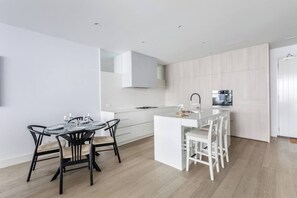 A modern kitchen with white cabinetry, a central island, and a dining area with black chairs. - Bayside Calm Walk to Mornington Foreshore and Dining (Mornington)