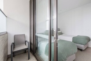 Ein modernes Schlafzimmer mit einer Schiebeglasdoor, einem Einzelbett mit grüner Bettwäsche und einem Sessel.