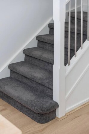 Una escalera con peldaños alfombrados y una barandilla blanca.
