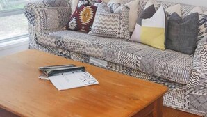 Un salon avec un canapé à motifs, une table basse en bois et deux œuvres d’art encadrées accrochées au mur.