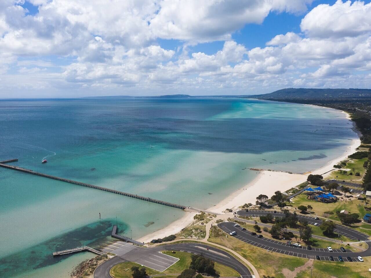 Luchtbeeld van een kustgebied met een strand, een pier en een parkeerplaats.
