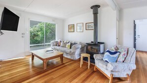 Un salon comprenant un canapé, une table basse, un petit tabouret, une cheminée et un téléviseur fixé au mur.