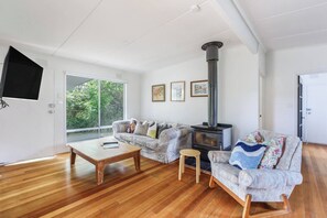 A living room with a sofa, a coffee table, a small stool, a fireplace, and a television mounted on the wall. - Bayside Cottage Leafy Stay near Rye Beach and Dining (Rye)