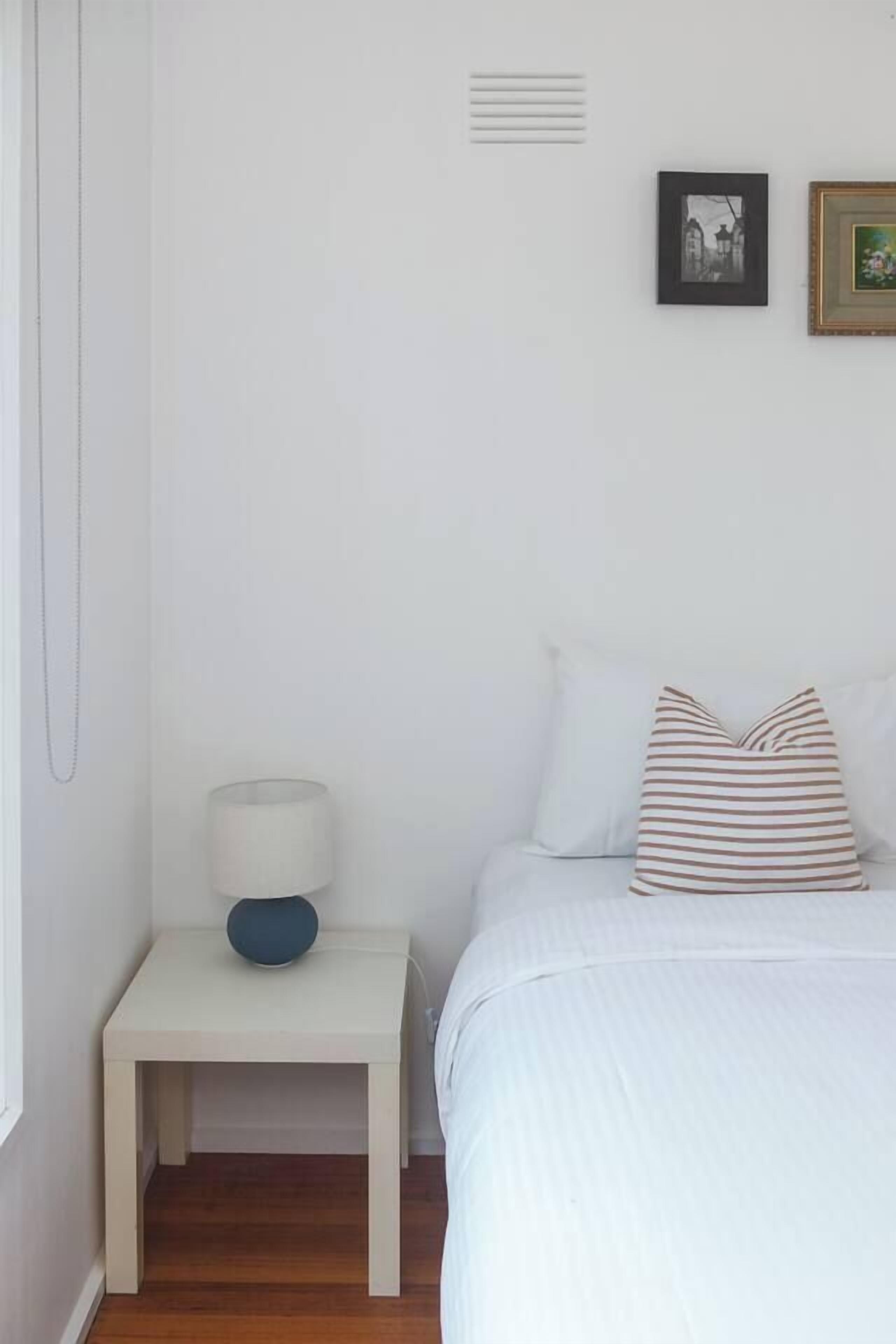 Een slaapkamer met een bed, nachtkastje, lamp en twee ingelijste foto’s aan de muur.
