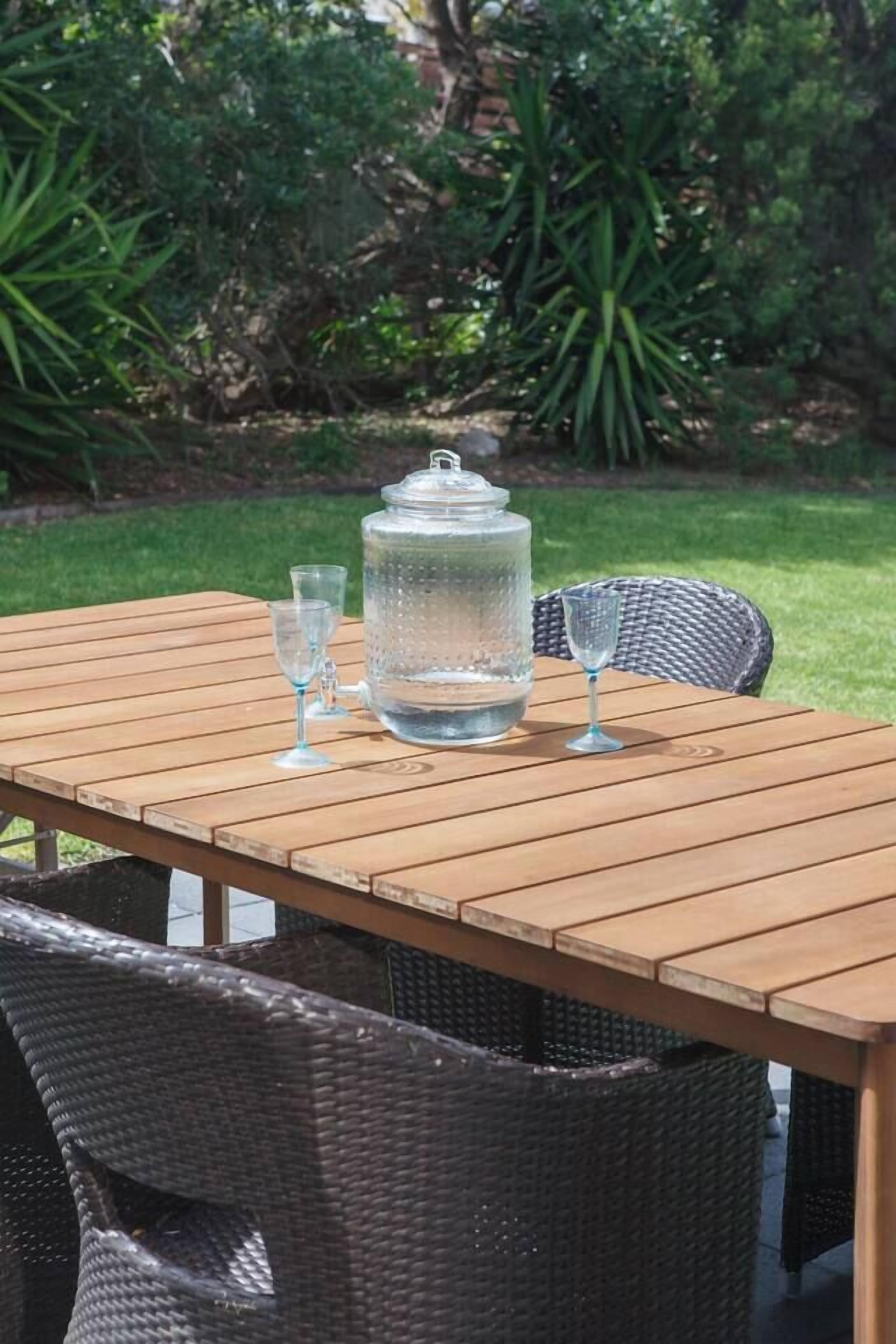 A wooden table with a water dispenser and glasses, surrounded by wicker chairs.