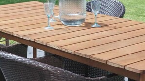 Une table en bois, agrémentée d’un distributeur d’eau et de verres, entourée de chaises en osier.