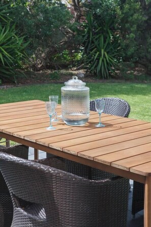 A wooden table with a water dispenser and glasses, surrounded by wicker chairs. - Bayside Cottage Leafy Stay near Rye Beach and Dining (Rye)
