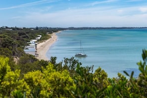 A coastal view with a beach, a sailboat, and a line of buildings along the shore. - Bayside Cottage Leafy Stay near Rye Beach and Dining (Rye)