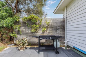 Ein Grill im Garten, mit Holzzaun und Kübelpflanzen.