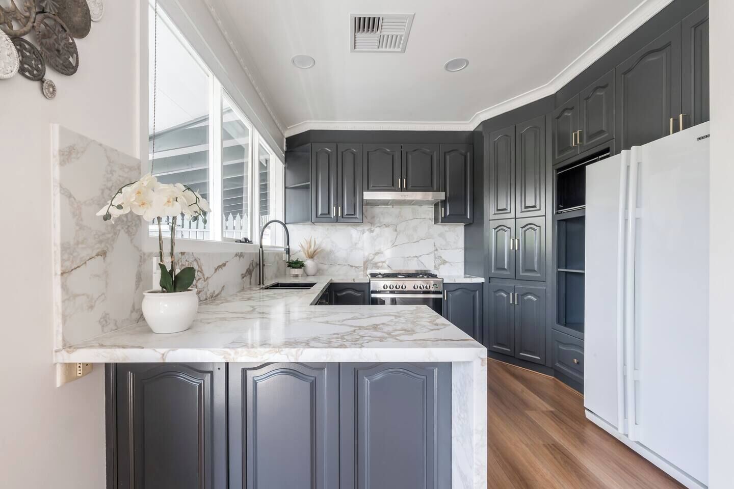 A kitchen with dark gray cabinets, a white marble countertop, a stainless steel sink, and a built-in stove.