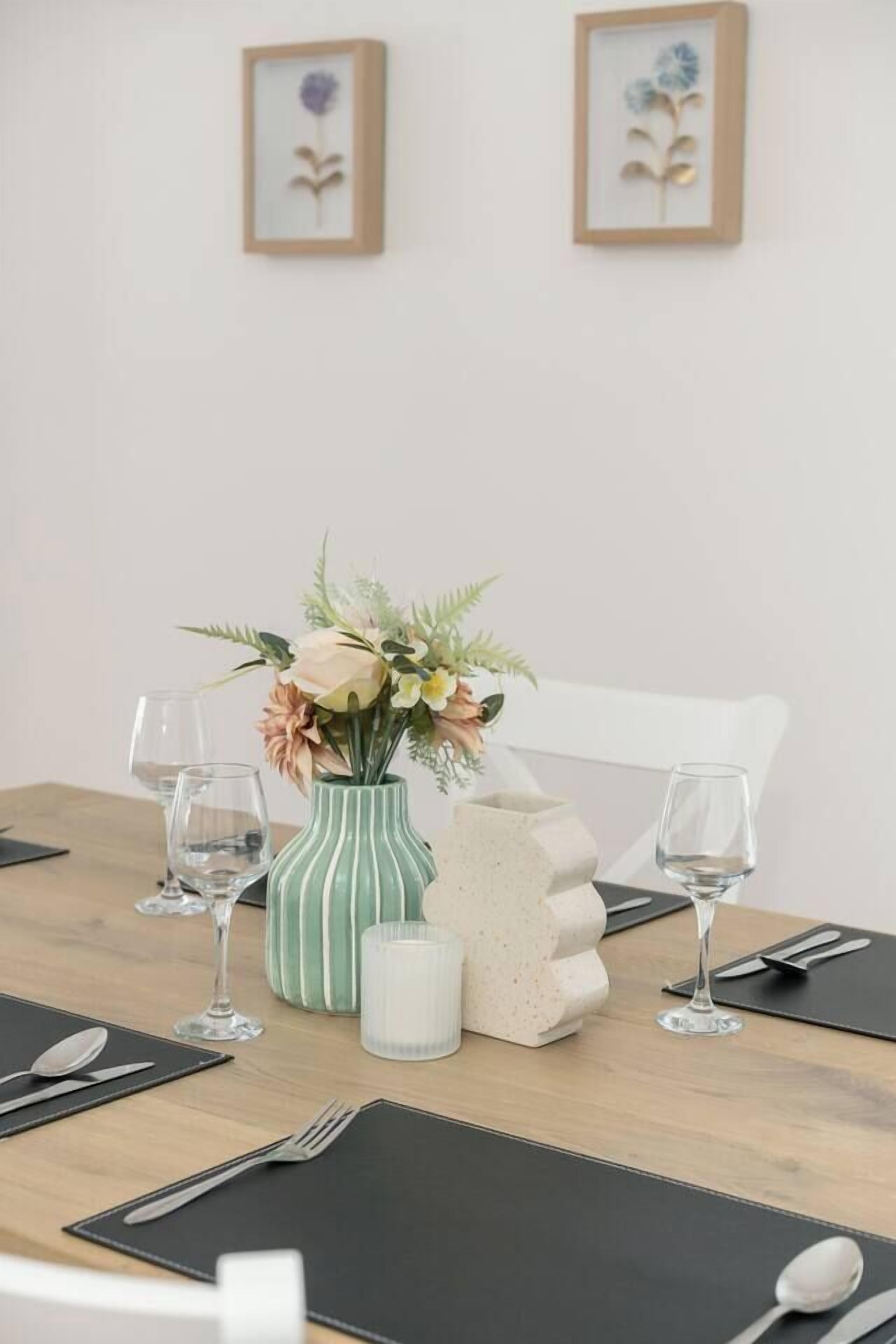 Une table à manger dressée avec un vase de fleurs, une bougie et un objet décoratif.